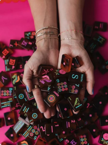 Two hands holding a pile of colourful American Mahjong tiles